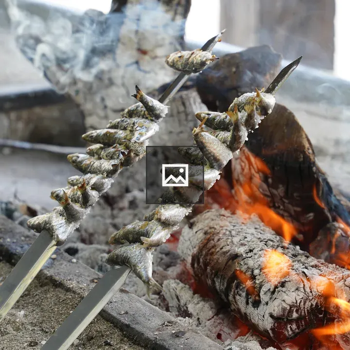 Two sardine skewers grilling over fire