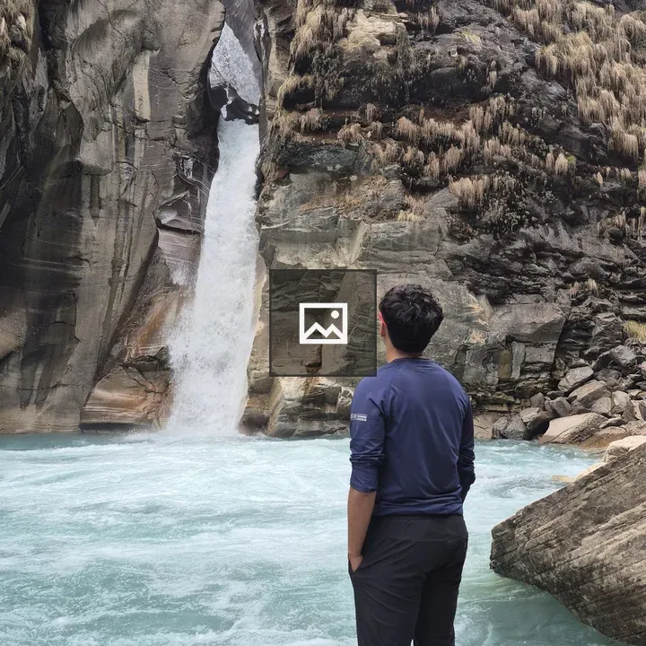 Person by Riverbank with Waterfall