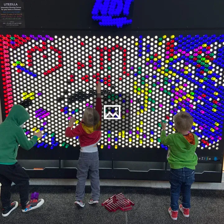 Three children designing a rainbow on a pegboard