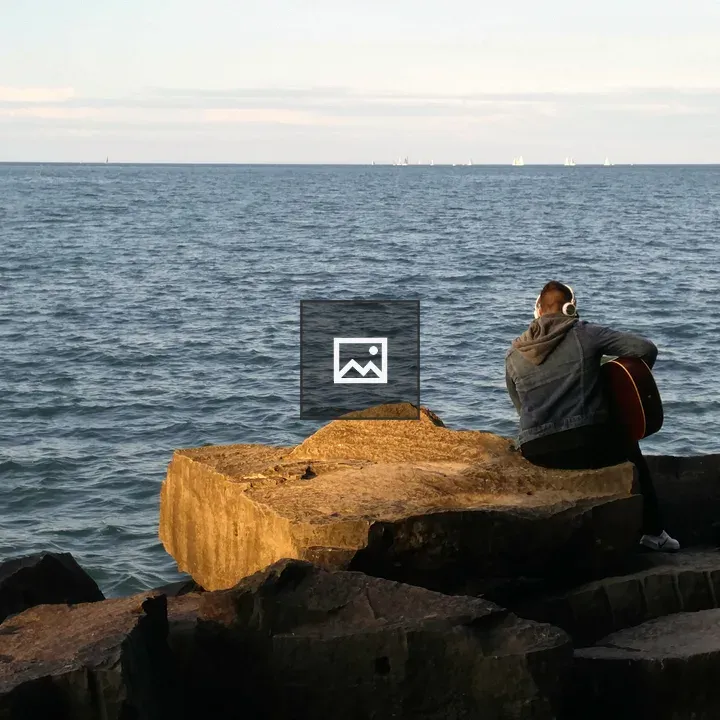 Person with guitar on rocky coast