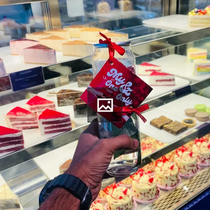 Hand Holding Bottle in Front of Pastry Display