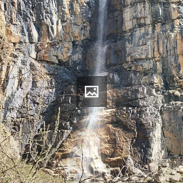Waterfall on rocky cliff in greenery