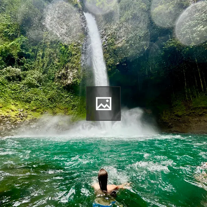 Person swimming toward waterfall in jungle gorge