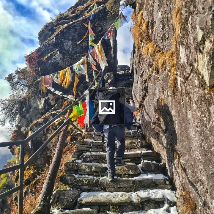 Person climbing narrow staircase beside prayer flags