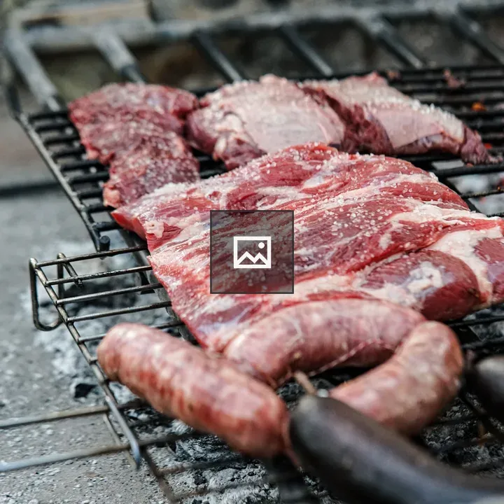Raw steaks and sausages on grill