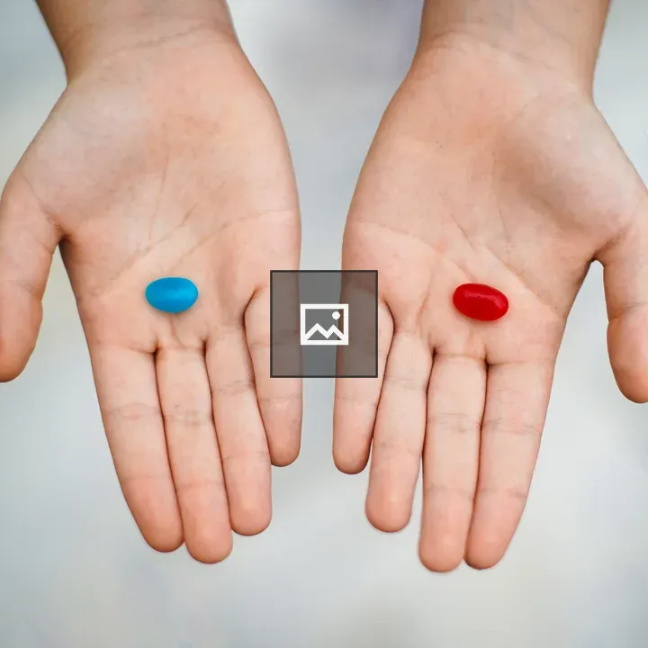 Two hands holding blue and red pills