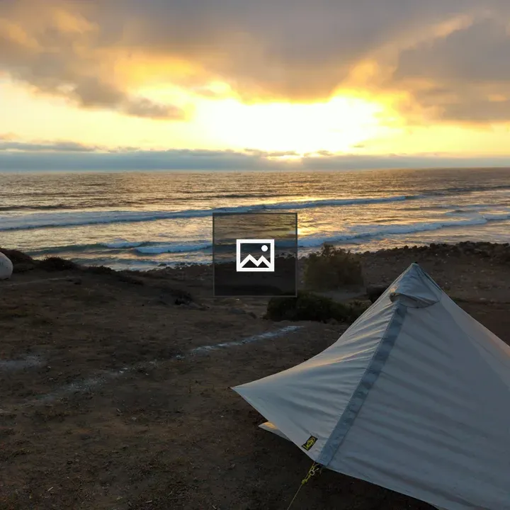 Grey tent on sea cliff at sunset